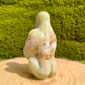 May include: A green, white, and orange carved stone sculpture of a person in a seated position.