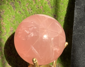 May include: A large, pink rose quartz sphere on a gold metal stand. The sphere is polished and has a translucent appearance.