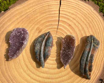 May include: Four amethyst crystal feathers with a purple and brown color scheme. The feathers are arranged on a wooden surface.