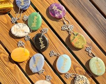 May include: A collection of gemstone pendants in various colors, including blue, green, purple, and yellow, each with a silver chain and a decorative clasp. The pendants have gold text and are displayed on a wooden surface.