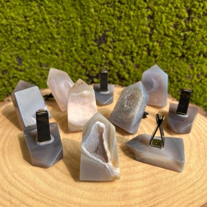 Puede incluir: Una colección de ocho ambientadores de coche de cristal de ágata gris con clips metálicos negros. Los cristales son de diversas formas y tamaños, algunos con un acabado druzy natural.