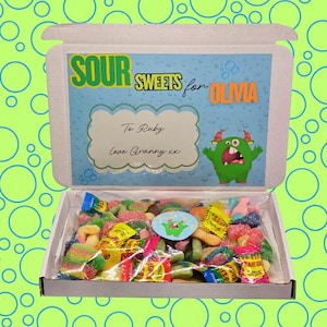 May include: A white box containing a selection of colourful sour sweets. The lid displays the text "SOUR SWEETS for OLIVIA" and a green monster illustration. The box is filled with various wrapped sweets and a monster sticker.