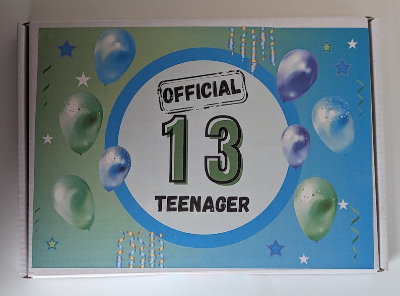 Op de afbeelding: Witte kartonnen doos met een blauw en groen ontwerp, met ballonnen en sterren. De tekst "OFFICIAL 13 TEENAGER" staat prominent in een cirkelvormig kader, wat wijst op een verjaardagsthema.