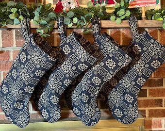 May include: A set of five navy blue Christmas stockings with a cream-colored geometric pattern. Each stocking has a loop for hanging and is displayed against a brick background, with greenery and decorations above.