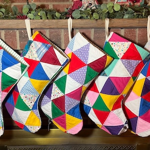 May include: Five quilted Christmas stockings hanging in a row, each constructed from a patchwork of multicolored fabric triangles. The stockings feature a vibrant array of solid colors, polka dots, and gingham patterns in red, blue, green, yellow, and pink.