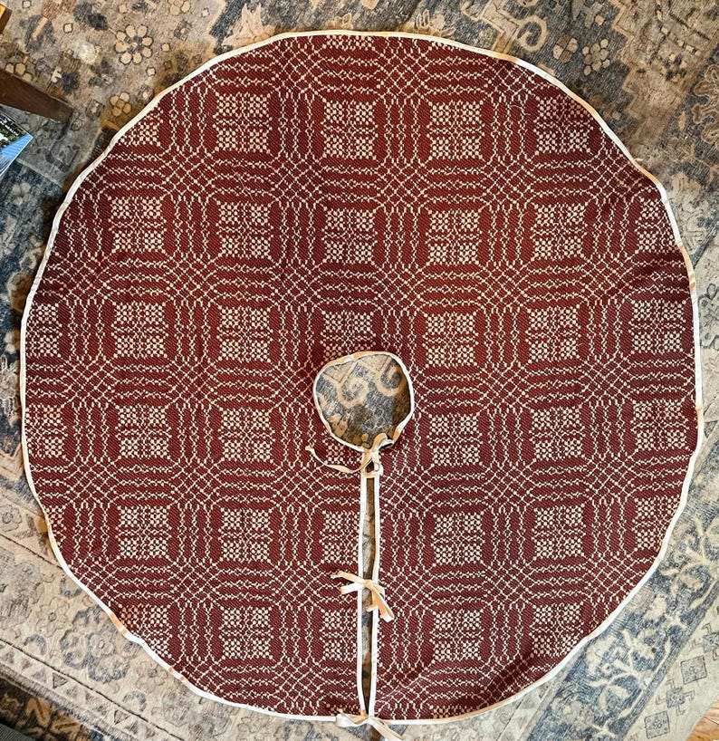 May include: A circular tree skirt featuring a deep red and white geometric woven pattern. The fabric has a white piped edge, a central circular cutout, and a straight slit opening secured with three sets of white fabric ties for closure.