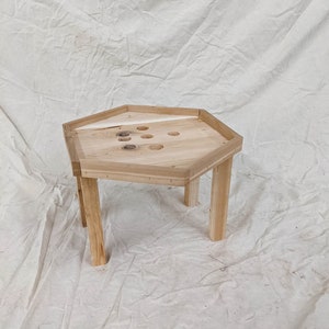 May include: A hexagonal wooden table with a light wood finish and six legs. The table top has a series of holes drilled into it.