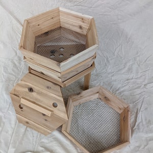 May include: A wooden hexagonal compost bin with a removable lid and a mesh screen inside. The bin is made of natural wood and has a rustic look.