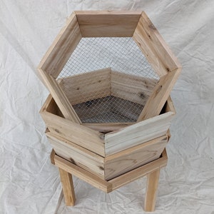 May include: A wooden hexagonal planter with three tiers and a wire mesh insert. The planter is on a stand with four legs.