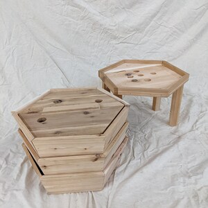 May include: A set of four wooden hexagonal nesting tables. The tables are made of natural wood and have a rustic finish. The top table has a small hole in the center.