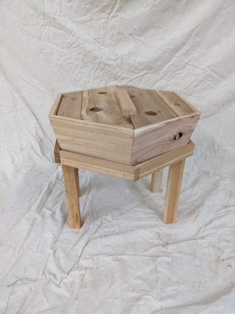 May include: A hexagonal wooden planter with a removable top and four legs. The planter is made of natural wood and has a rustic appearance.