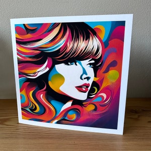 May include: A colorful pop art print featuring a woman's portrait. The artwork showcases a woman with blue eyes, red lips, and vibrant, flowing hair in shades of pink, orange, yellow, and blue. The print is set against a white background.