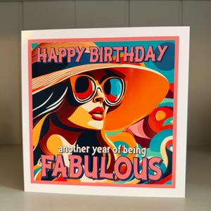 May include: Birthday greeting card with a colorful illustration of a woman wearing sunglasses and a large orange hat. The card reads "HAPPY BIRTHDAY" and "another year of being FABULOUS" in a retro font.