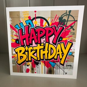 May include: A white greeting card featuring a vibrant graffiti design. The words "HAPPY BIRTHDAY" are prominently displayed in bold, colourful lettering, with red, yellow, and blue accents. The background has a textured, urban aesthetic with paint splatters.