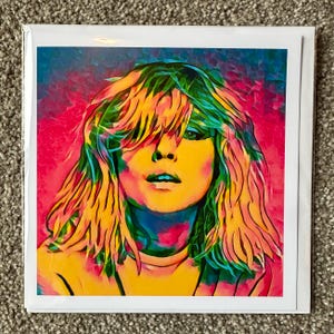 May include: A colorful art print featuring a portrait of a woman with long, layered blonde hair. The artwork uses vibrant hues of yellow, pink, blue, and green. The print is on a white card, perfect for framing or gifting.