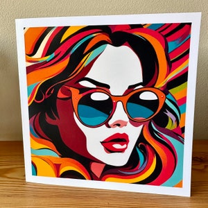 May include: A colorful pop art print featuring a woman wearing orange sunglasses with blue lenses. Her hair is a vibrant mix of red, orange, yellow, and blue. The artwork is set against a white background.