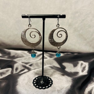 May include: Silver earrings with a spiral design and a dangling blue gemstone.