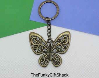 May include: A gold-toned metal butterfly keychain with intricate details. The butterfly is attached to a silver chain and a silver key ring.