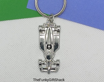 May include: Silver-toned metal keychain featuring a detailed model of a race car. The keychain has a silver ring for attaching to keys.