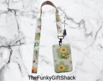 May include: A white lanyard with a floral pattern and a matching white card holder with a floral pattern. The lanyard has a black clip and a black swivel hook.