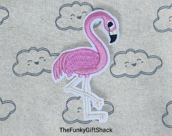 May include: Pink embroidered flamingo patch with white stitching. The patch is on a light gray fabric background with gray embroidered clouds.
