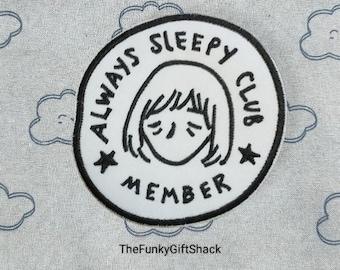 May include: White embroidered patch with black text that reads "Always Sleepy Club Member" and a cartoon drawing of a person with their eyes closed. The patch is on a gray fabric background with a cloud pattern.