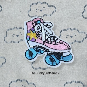 May include: Pink and white roller skate with a yellow star embroidered on the side. The skate is on a light brown fabric background with a repeating pattern of white clouds with smiling faces.