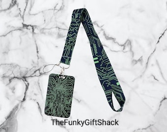 May include: A black and green lanyard with a circuit board design. The lanyard has a matching black and green ID badge holder with a silver clip.