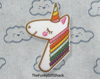 May include: White unicorn head embroidered patch with a rainbow mane and a gold horn. The unicorn is on a light gray background with white clouds.