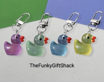 May include: Four rubber duck keychains in different colors: purple, green, blue, and yellow. Each duck has a red beak and a silver keychain.
