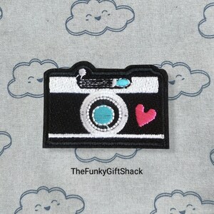 May include: Black and white embroidered iron-on patch of a vintage camera with a red heart. The text "TheFunkyGiftShack" is below the image.