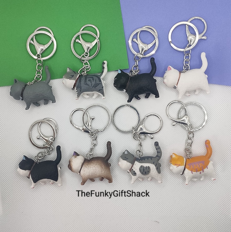 Puede incluir: Un conjunto de ocho llaveros de gato con diferentes colores de pelaje y patrones. Cada llavero tiene un anillo de llave plateado y una peque&ntilde;a figura de gato detallada.