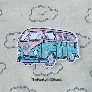May include: A light blue and pink embroidered patch of a vintage Volkswagen van with peace signs and flowers. The van is on a beige fabric background with clouds.