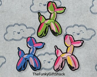 May include: Three embroidered iron-on patches of balloon animal dogs in different colors. The patches are on a light blue fabric with a cloud pattern. The dogs are pink and yellow, blue and pink, and green and pink.
