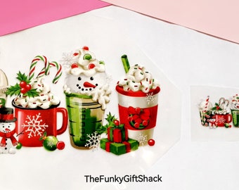 May include: A digital design featuring five festive holiday drinks with whipped cream, candy canes, and snowflakes. The drinks include a green smoothie, a red mug, a green iced coffee, a red and white hot chocolate, and a green iced coffee with a snowman face. The design includes the text "TheFunkyGiftShack".