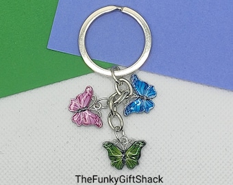 May include: A silver key chain with three butterfly charms. The butterflies are pink, blue, and green.