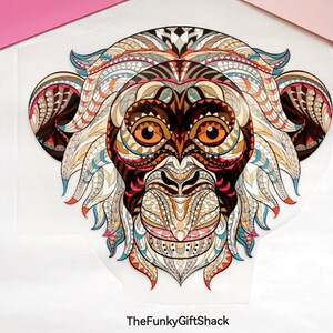 May include: A colourful, intricate design of a monkey's face with geometric patterns in shades of brown, orange, blue, pink, and white.