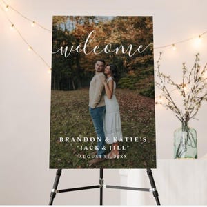 May include: A welcome sign with a photo of a couple in a forest setting. The sign includes the word "welcome" in cursive, and the names "Brandon & Katie's" with the phrase "Jack & Jill" and a date.