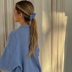 May include: A woman with long blonde hair wearing a light blue shirt with a ponytail held in place with two blue scrunchies.