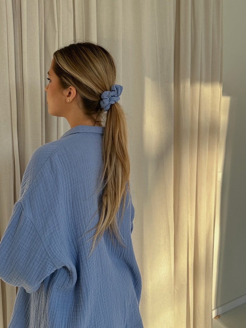 May include: A woman with long blonde hair wearing a light blue shirt with a ponytail held in place with two blue scrunchies.