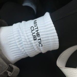 May include: White socks with black text that reads "AESTHETIC CLUB".