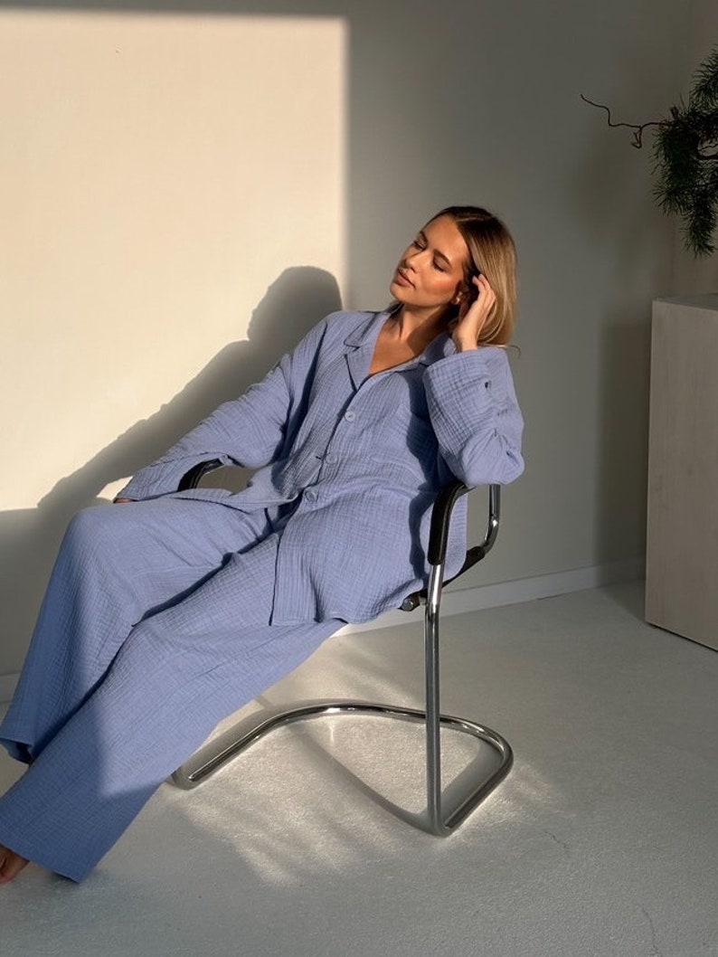 May include: A person wearing a light blue pajama set with a button-up top and wide-leg pants. The person is sitting on a silver chair in a room with white walls.
