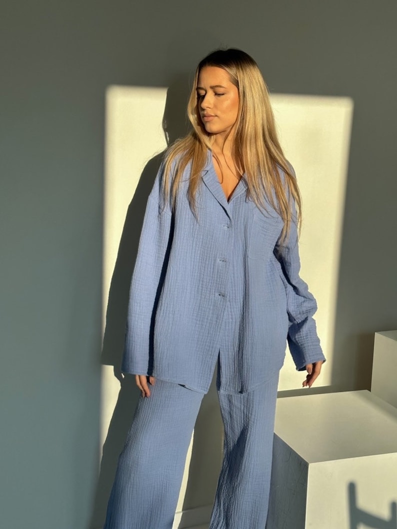 May include: A light blue pajama set with a long-sleeved shirt and wide-leg pants. The shirt has a button-up front and a pocket on the left side.