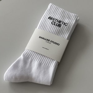 May include: White socks with black text that reads "Aesthetic Club" and "Shallke Studio Lithuania" with the website address "www.shallke.lt".