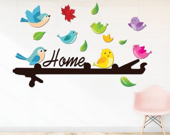 Könnte beinhalten: Ein Set aus bunten Vogel- und Blatt-Wandaufklebern mit dem Wort "Home" in schwarzer Schrift. Die Aufkleber sind an einer weißen Wand mit einem rosa Stuhl im Vordergrund angebracht.
