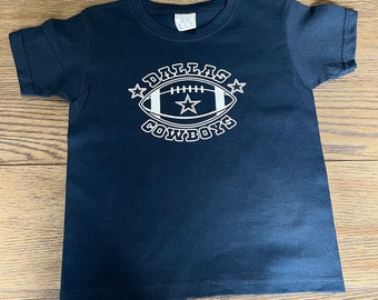 May include: A black t-shirt with a white graphic of a football and the words "Dallas Cowboys" in a circle.