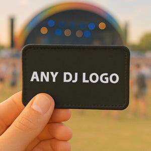 May include: A rectangular black patch with the text "ANY DJ LOGO" in white. The patch is held up in front of a blurred outdoor scene with a stage and a rainbow-colored structure.