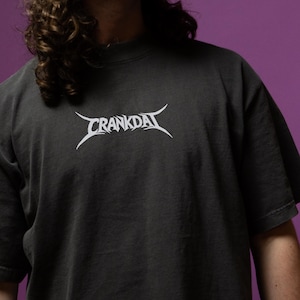May include: Dark gray t-shirt with the word "CRANKDAT" in white, stylized, gothic lettering across the chest. The shirt has a crew neck and short sleeves. The fabric appears to be a soft cotton blend.