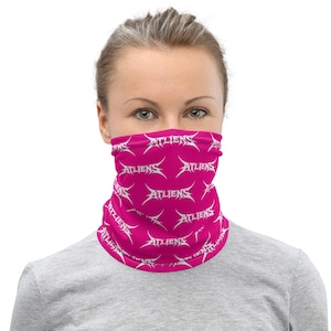 May include: A pink face covering with a repeating white "ATLIENS" text design. The face covering is worn around the neck and covers the lower face. The person is wearing a gray shirt.