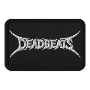 May include: A rectangular black embroidered patch featuring the word DEADBEATS in a stylized, sharp, white metallic-looking font. The text is centered on the black fabric background, which has a thick, stitched border around the entire edge.